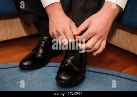 Der Typ bindet die Schnürsenkel auf schwarzen klassischen Schuhen. Der Bräutigam trägt schöne Schuhe und bindet seine Schnürsenkel Stockfoto