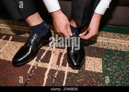 Der Typ bindet die Schnürsenkel auf schwarzen klassischen Schuhen. Der Bräutigam trägt schöne Schuhe und bindet seine Schnürsenkel Stockfoto