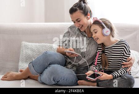 Fröhliche Mutter und Tochter ruhen zu Hause und hören Musik über Kopfhörer. Das Konzept einer glücklichen Familie und freundschaftlichen Beziehungen. Stockfoto