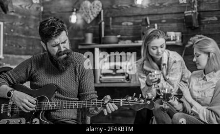 Mann mit langen buschigen Bart singen leidenschaftlich, Musikkonzept. Mädchen trinken Tee oder Wein und genießen schöne Melodien. Bärtiger Mann spielt Gitarre Stockfoto