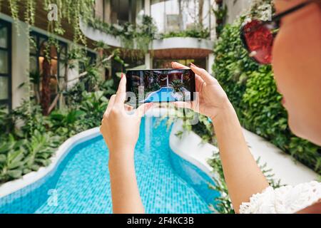 Hände der weiblichen Touristen, die Foto von Schwimmbad in Luxuriöses Spa-Resort auf dem Smartphone, um in den sozialen Medien zu posten Stockfoto