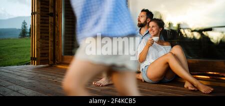 Familie mit kleiner Tochter sitzt auf der Terrasse der Holzhütte, Urlaub in der Natur Konzept. Stockfoto