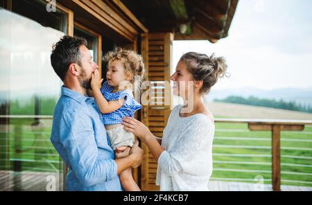 Familie mit kleiner Tochter auf der Terrasse der Holzhütte, Urlaub in der Natur Konzept. Stockfoto