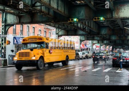 New York City, USA. Gelber Schulbus fährt durch den Regen unter einer erhöhten U-Bahn-Strecke an der Roosevelt Ave, Queens. Stockfoto