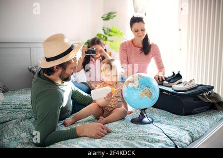 Familie mit zwei kleinen Töchtern, die für den Urlaub auf dem Bett zu Hause packen. Stockfoto