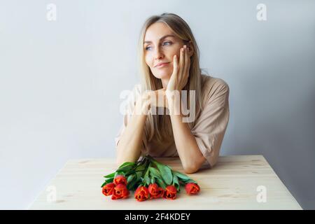 Junge charmante Frau sitzt nachdenklich mit einem Blumenstrauß. Stockfoto