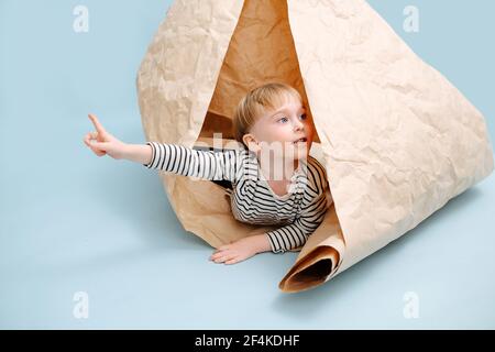 Verspielt blonde Junge in einem gerollten Packpapier liegen. Er zeigt mit dem Finger auf die Seite und schaut auf jemanden. Er trägt gestreiftes Langarm-Shirt. Studi Stockfoto