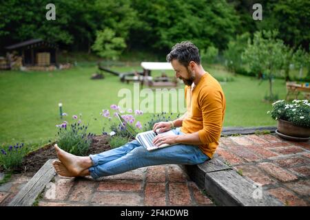 Reifer Mann mit Laptop im Garten arbeiten, Green Home Office Konzept. Stockfoto