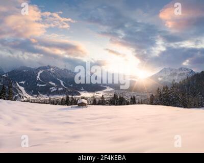 Schöne Winterszene mit schneebedeckter Wiese und Holzhütte Im Vordergrund - Tal mit Garmisch-Partenkirchen Dorf und Alpen Berge Zurück Stockfoto