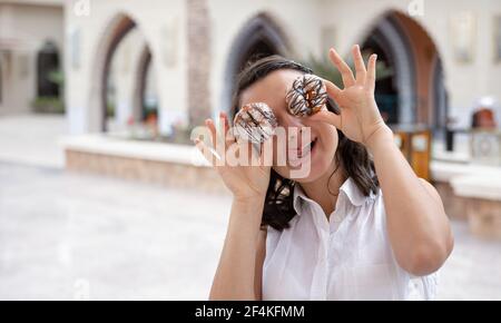 Lustige Mädchen posiert mit Donuts in ihren Händen im Sommer draußen. Urlaubs- und Urlaubskonzept. Stockfoto