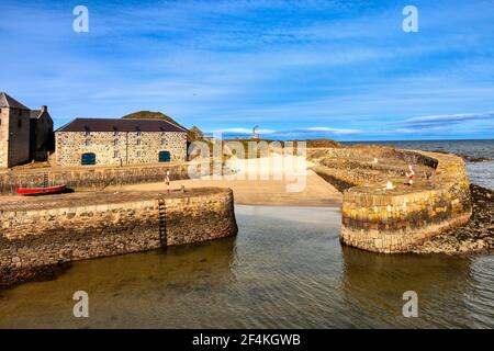 PORTSOY ALTER HAFEN MORAY FIRTH ABERDEENSHIRE SCHOTTLAND GELBE FLECHTEN WACHSEN AUF STEINBLÖCKEN IN DER WAND EIN SANDSTRAND UND EIN ROTES BOOT Stockfoto