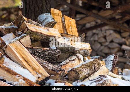 Stapel oder Stapel aus Blöcken, Stücken oder Holzstämmen im Winter oder Frühjahr mit Schnee. Stapelholz zum Trocknen und Lagern Stockfoto