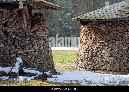 Kreisförmige oder zylindrische Struktur oder Stapel aus Blöcken, Stücken oder Baumstämmen aus Holz und Dach im Winter oder Frühjahr mit Schnee. Holz stapeln Stockfoto