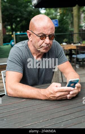 Tilburg, Niederlande. Baldign Mann liest seine Smartphone beim Sitzen auf einem Restaurant-Terrasse-Tisch. Stockfoto