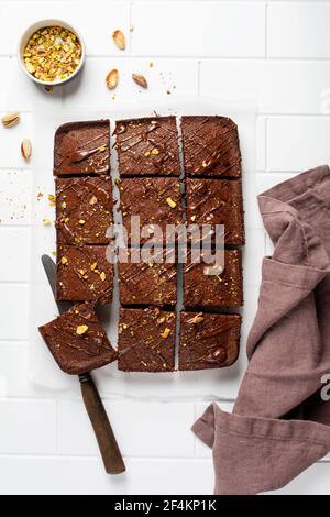 Schokoladenquadrate mit Pistazien und Erdbeeren auf weißem Papier auf hellem Hintergrund, Draufsicht, horizontale Komposition. Flache Lebensmittel Stockfoto