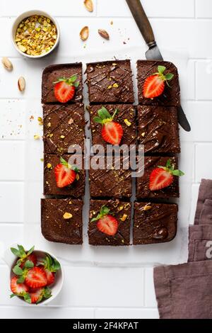 Schokoladenquadrate mit Pistazien und Erdbeeren auf weißem Papier auf hellem Hintergrund, Draufsicht, horizontale Komposition. Flache Lebensmittel Stockfoto