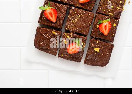 Schokoladenquadrate mit Pistazien und Erdbeeren auf weißem Papier auf hellem Hintergrund, Draufsicht, horizontale Komposition. Flache Lebensmittel Stockfoto