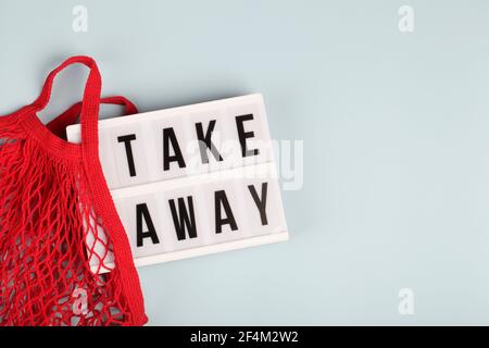 Leuchtkasten mit Text wegnehmen in roten Mesh-Tasche auf blauem Hintergrund , Wiedereröffnung, online, Lieferkonzept Stockfoto