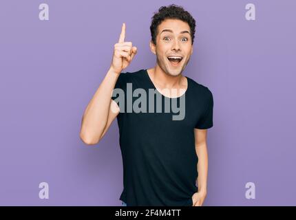 Junger schöner Mann trägt lässige schwarze T-Shirt zeigt Finger nach oben mit erfolgreicher Idee. Verlassen und glücklich. Nummer eins. Stockfoto