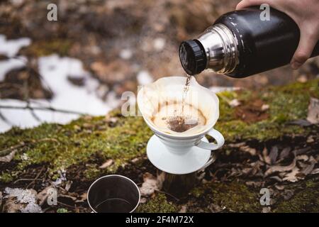 Brauen Gießen Sie über Kaffee in der Natur bei einem Wanderausflug. Heißes, dampfendes Wasser von Hand in einen Papierfilter gießen Stockfoto