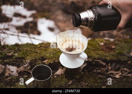 Brauen Gießen Sie über Kaffee in der Natur bei einem Wanderausflug. Heißes, dampfendes Wasser von Hand in einen Papierfilter gießen Stockfoto