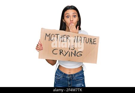 Junge hispanische Mädchen hält Mutter Natur weint Protest Karton Banner über Mund mit Hand, schockiert und Angst vor Fehler. Überrascht expre Stockfoto