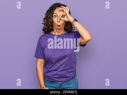 Mittelalter hispanische Frau trägt Freizeitkleidung tun ok Geste schockiert mit überrascht Gesicht, Auge durch die Finger schauen. Ungläubiger Ausdruck. Stockfoto