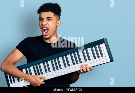 Junger afroamerikanischer Mann hält Klavier Keyboard wütend und verrückt schreien frustriert und wütend, schreien vor Wut. Wut und aggressives Konzept. Stockfoto
