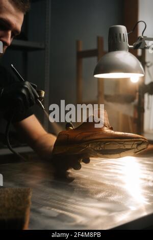 Nahaufnahme Hände von nicht erkennbaren Schuster tragen schwarze Handschuhe Sprühen Farbe von hellbraunen Lederschuhe. Stockfoto