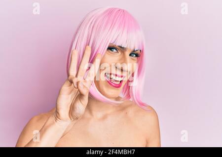 Junger Mann trägt Frau Make-up trägt rosa Perücke zeigt und zeigt mit den Fingern Nummer drei, während lächelnd zuversichtlich und glücklich. Stockfoto