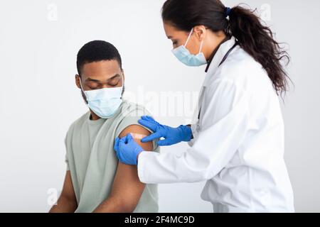 Arzt, der Gips auf den Arm des Mannes nach der Impfung anwendet, weißer Hintergrund Stockfoto