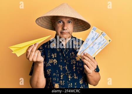 Mittelalter kahler Mann trägt traditionelle asiatische Hut halten Bordkarte entspannt mit ernsten Ausdruck auf Gesicht. Einfach und natürlich auf die Cam Stockfoto