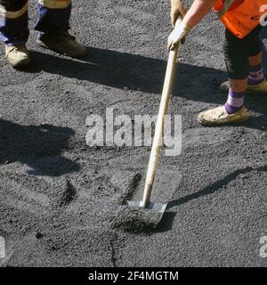 Straßenreparaturarbeiten. Arbeiter gleichen den Asphalt mit Schaufeln. Bauarbeiter während der Asphaltstraße. Handarbeit im Bauwesen Stockfoto