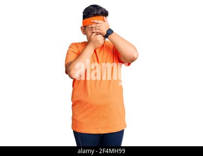 Kleiner Junge Kind trägt Sportkleidung, die Augen und Mund mit Händen bedeckt, überrascht und schockiert Stockfoto