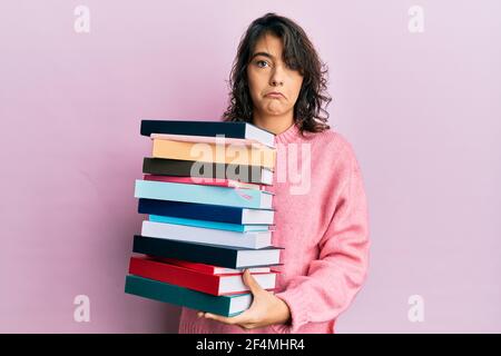 Junge hispanische Frau hält einen Stapel von Büchern deprimiert und sorgen für Not, Weinen wütend und Angst. Trauriger Ausdruck. Stockfoto