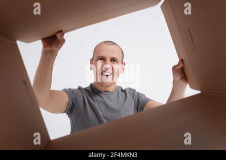 Glücklich lächelnder Mann Auspacken und Öffnen einer Karton-Geschenkbox und Blick nach innen. Ansicht aus der Box Stockfoto