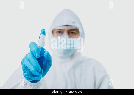 Der Arzt hält eine Alkoholflasche und trägt persönliche Schutzausrüstung oder psa, Maske, Brille, medizinische Handschuhe und Anzug zum Schutz COVID-19 infe Stockfoto