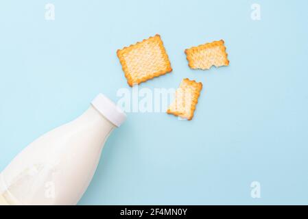 Zerbrochene trockene Kekse und eine Flasche Milch auf blauem Hintergrund, Draufsicht, Layout. Konzeptbild über Essen und Frühstück Stockfoto