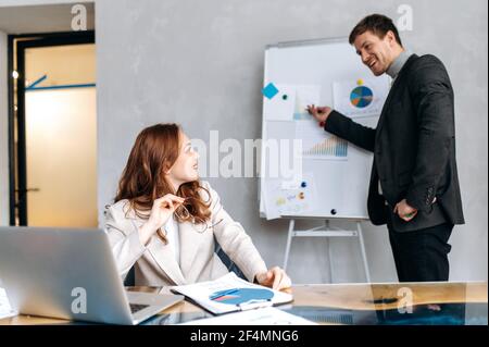 Schöner stilvoller Mann in formellen Anzug eine Präsentation auf Konferenz, diskutieren neue Geschäftsstrategie. Attraktive männliche Mitarbeiter senden Arbeitsbericht an schöne rothaarige Frau Chef Stockfoto