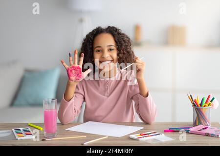 Fröhliche afroamerikanische Mädchen malen und zeigen bunte Hand, Ruhe zu Hause Stockfoto
