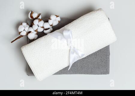 Nahaufnahme von oben eines Stapels aufgerollter weißer und grauer Handtücher mit einem Baumwollzweig. Stockfoto