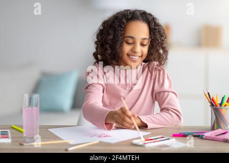 Quarantäne-Freizeit. afroamerikanische Mädchen Zeichnung auf Papier mit Farben, Ruhe zu Hause Stockfoto