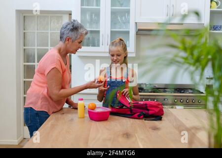 Ältere kaukasische Großmutter gab der Enkelin ein Lunchpaket und Obst Küche Stockfoto