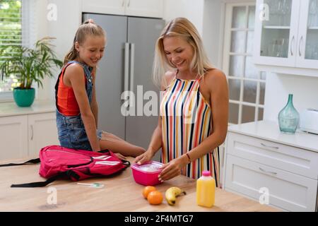 Lächelnde kaukasische Mutter bereitet Tochter Lunchpaket in der Küche Stockfoto