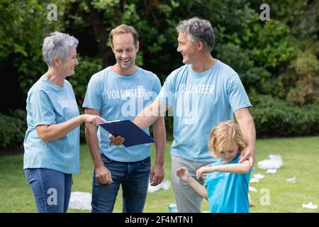 Kaukasisches Seniorenpaar mit Clipboard und Mann und Sohn im Volunteer-Shirts im übersäten Feld Stockfoto