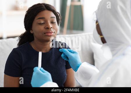 Arzt in Schutzanzug nimmt Tupfer zum Patienten zu Hause Stockfoto