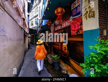 Eine Frau in orangefarbener Kleidung geht in Chinatown, Bangkok, Thailand eine kleine Gasse mit Wänden entlang, die mit Street Art bedeckt sind Stockfoto