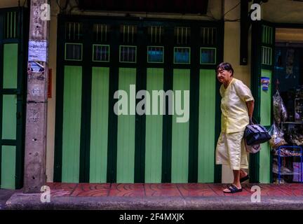 Eine ältere Frau, in chinesischer Kleidung gekleidet, geht an einem grünen Facadegebäude in Chinatown, Bangkok, Thailand vorbei Stockfoto