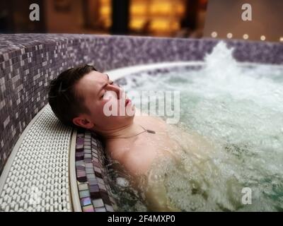 Ein Mann liegt in einem sprudelnden Whirlpool in einem Spa-Hotel und entspannt sich im Pool. Stockfoto