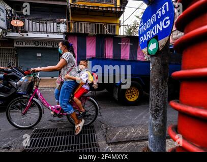 Eine Radfahrerin, mit einem jungen Schuljungen Beifahrer, fährt ihr Fahrrad entlang einer schmalen Soi in Talat Noi, Bangkok, Thailand Stockfoto